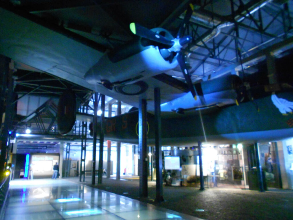Muzeum Powstania Warszawskiego w Warszawie. Pomieszczenie z repliką samolotu podwieszoną pod sufitem. Niebieskie światła. 